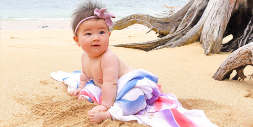 Baby Luna on a beach with a bow in her hair and a swaddle around her legs