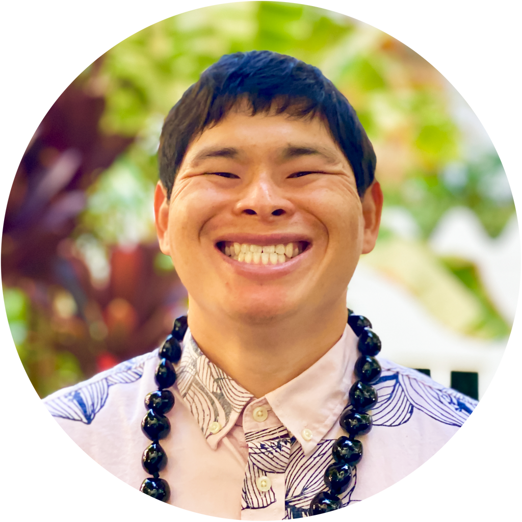 Chris wears an aloha shirt and kukui nut lei, blurred floral background
