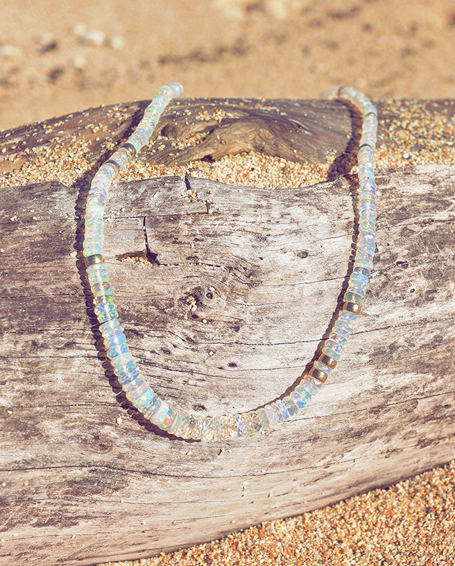 opal necklace on a piece of driftwood on a sandy beach