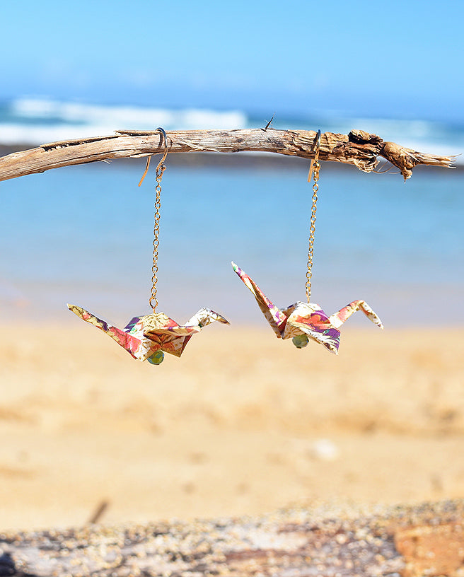 purple crane earrings with the ocean in the background